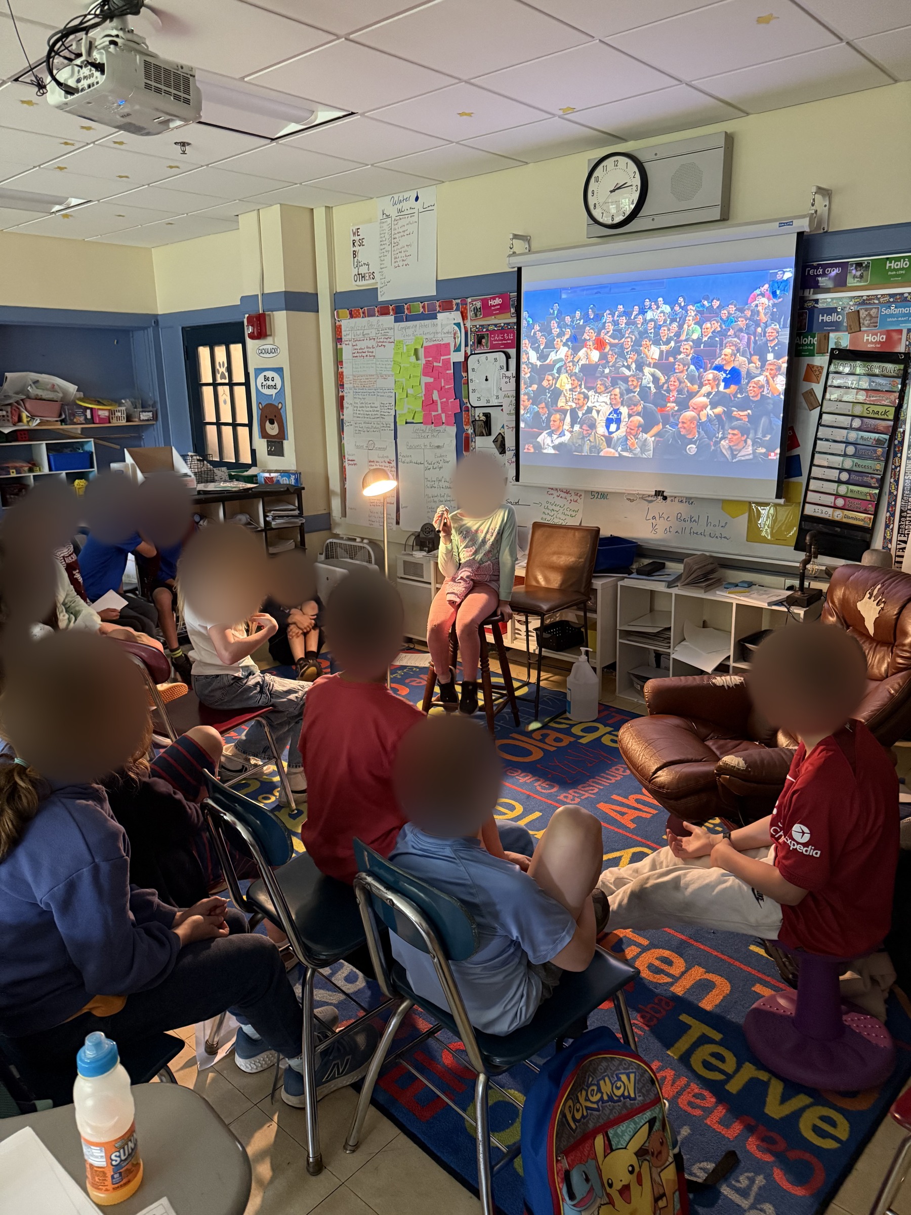 A student performs at the microphone while classmates gather for a classroom comedy event