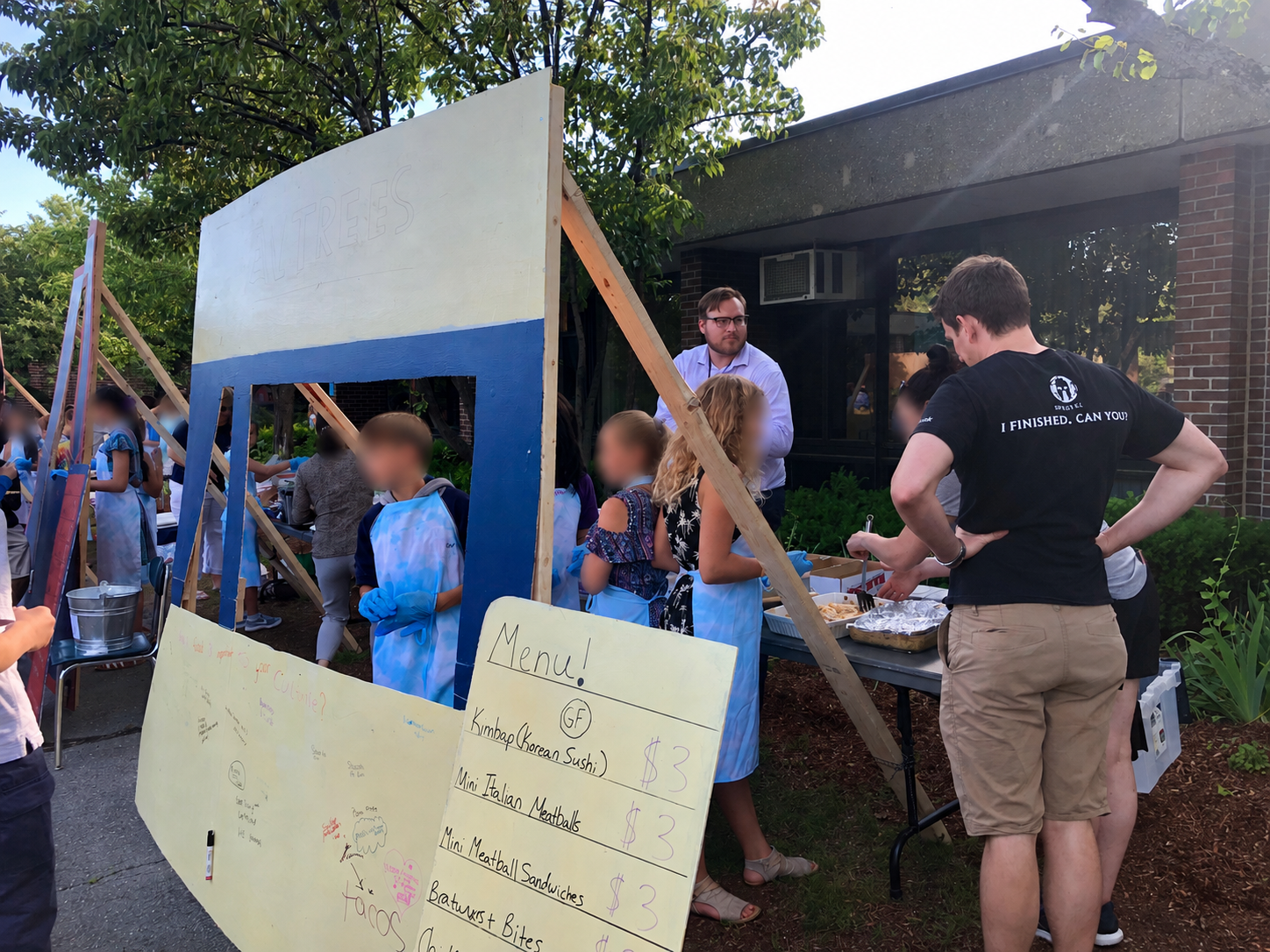 Students serving food beside a handwritten menu at their food-truck exhibition